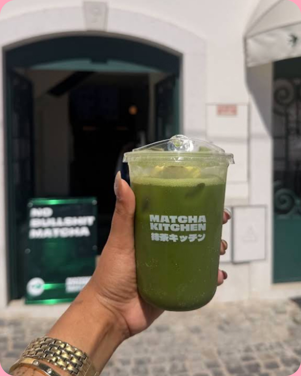 A hand holding a Matcha Kitchen iced matcha in front of the café door