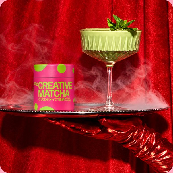Matcha cocktail in a coupe glass next to a Creative Matcha jar, on a red velvet stage