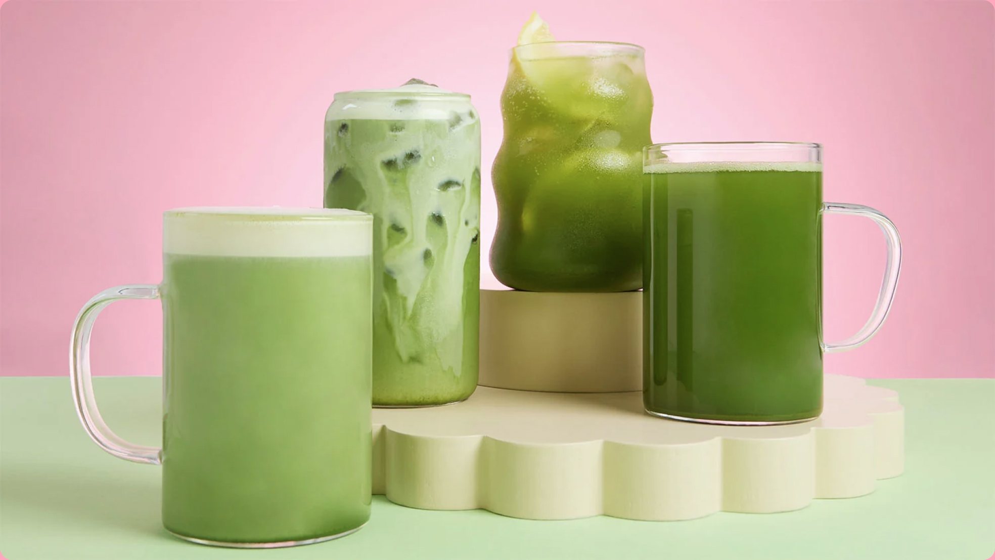 Two glasses of iced matcha latte on a pastel pedestal
